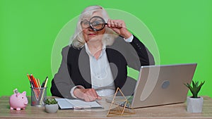 Investigator senior businesswoman hold magnifying glass near face looking with big zoomed funny eye