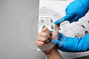 Investigator taking fingerprints of suspect on grey background, closeup with space for text