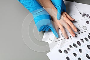 Investigator taking fingerprints of suspect on grey table, closeup.