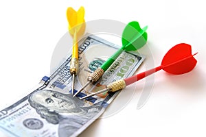 Investing with darts in yellow, green and red colors on a white background and 100 US dollars, and dollars for an accurate