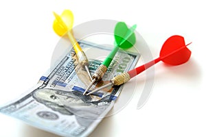 Investing with darts in yellow, green and red colors on a white background and 100 US dollars, and dollars for an accurate