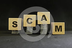 Investment scam, fraud and Ponzi scheme concept. Stack of coins on wooden blocks with word fraudulent in dark black background.