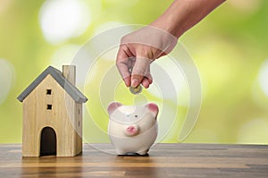 Investor hand hold a coin with save in the piggy bank put on the money on home model for family background.