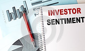 INVESTOR SENTIMENT text on a notebook with pen on a chart background