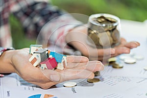 Investor show hand holding a model home and coin , Saving money