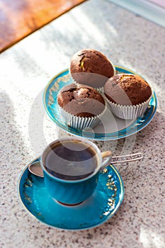 Invigorating cup of coffee with cupcakes is on the table for breakfast