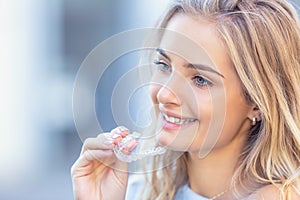 Invisalign orthodontics concept - Young attractive woman holding - using invisible braces or trainer photo