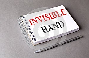 INVISIBLE HAND word on notebook on grey background