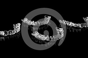 Invisible orthodontics cosmetic brackets on black background, tooth aligners, plastic braces. Modern teeth retainers created on a
