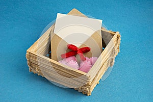 Invitation envelope in wooden wicker basket decorated with pink hearts on blue background.