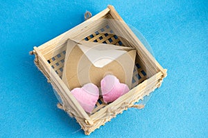 Invitation or love letter in old wooden wicker with plush hearts on blue background.