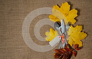 Invitation to dinner.  Spoon, fork, knife, autumn maple leaves and mountain ash on a textile background.