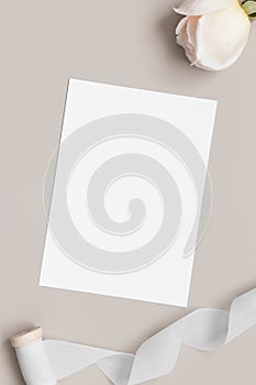 Invitation white card mockup with a rose and a satin tape on a beige table. 5x7 ratio, similar to A6, A5