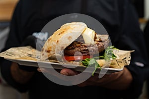 Inviting meat cheeseburger with white and red sauce and lettuce on table with beer and potato fries in the background. Delicious