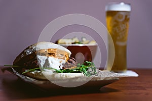 Inviting meat cheeseburger with white and red sauce and lettuce on table with beer and potato fries in the background. Delicious