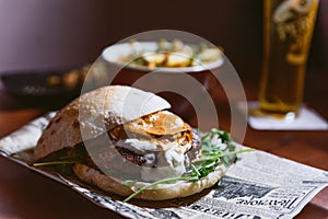 Inviting meat cheeseburger with white and red sauce and lettuce on table with beer and potato fries in the background. Delicious