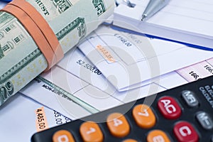 Invoices and bills, roll of dollar banknotes, calculator, closeup