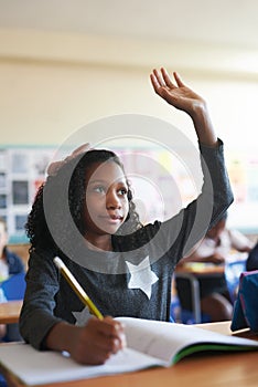 Involvement is important from an early age. a young girl sitting in her school classroom and raising her hand to answer