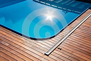 Ipe wood decking around the pool, edge of the outdoor swimming pool with sun reflection on the blue water