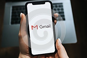 Hand holding iPhone with Gmail app logo on the screen.