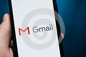 Hand holding iPhone with Gmail app logo on the screen.