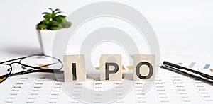 IPO word concept written on wooden blocks, cubes on a light table with flower ,pen and glasses on the chart background