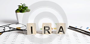 IRA word concept written on the wooden blocks, cubes on a light table with flower ,pen and glasses on chart background