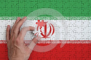 Iran flag is depicted on a puzzle, which the man`s hand completes to fold