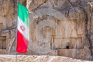 Iranian flag with ancient necropolis Naqsh-e Rustam in Fars province, Iran in background