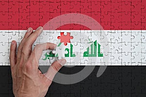 Iraq flag is depicted on a puzzle, which the man`s hand completes to fold