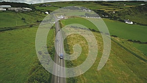 Ireland rural road aerial shot: cars riding near crossway. Cottages, meadows, fields on hills