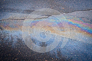 Iridescent spot of gasoline on the road with tire tracks.