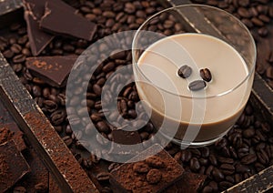 Irish cream baileys liqueur in glass with coffee beans and powder with dark chocolate in wooden tray on dark wood background