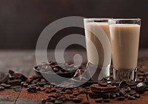 Irish cream baileys liqueur in shot glasses with coffee beans and powder with dark chocolate on dark wood background