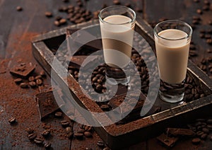 Irish cream baileys liqueur in shot glasses in wooden tray with coffee beans and powder on dark wood background