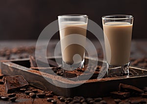 Irish cream baileys liqueur in shot glasses in wooden tray with coffee beans and powder on dark wood background