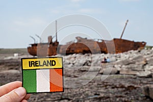 Irish flag and sign Ireland in focus. Plassey shipwreck on shore of Inisheer island. Aran islands, county Galway, Ireland out of