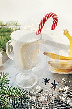 Irish traditional winter cream cocktail eggnog in a glass mug with milk, rum and cinnamon, banana covered with whipped cream,