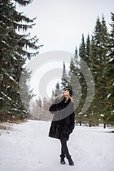 irl in a black hat and a fur coat stands on a snowy winter alley