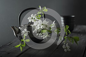 Iron asian teapot with branch of cherry flowers next to cup of tea on wooden background.