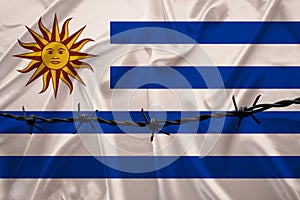 Iron barbed wire on the silk national flag of Uruguay with beautiful folds, the concept of a ban on tourism, political repression