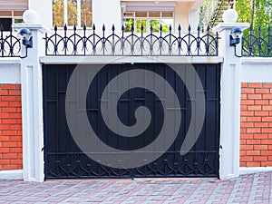 Iron black gate with a wrought pattern and sharp tips at the top and with a brick fence. Protected private area