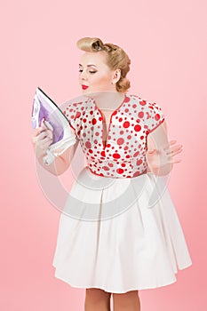 Iron and blonde woman in pin-up make up and hair dress. Girl looks on iron in hand makes selfy