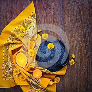 Iron blue teapot with yellow daisy flowers and candles on wooden background.