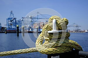 A iron bollard with a tied rope on a quay in the Port of Rotterdam in the Netherlands. In the background, slightly out of focus,