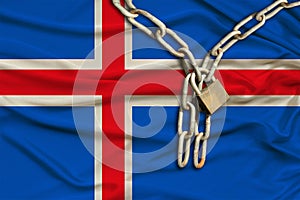 Iron chain and castle on iceland silk national flag with beautiful folds, the concept of a ban on tourism, political repression,