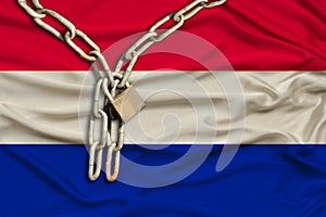 Iron chain and castle on the silk national flag of the Netherlands with beautiful folds, the concept of a ban on tourism,