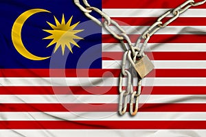 Iron chain and lock on Malaysia silk national flag with beautiful folds, the concept of a ban on tourism, political repression,