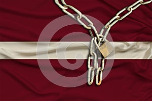 Iron chain and lock on the silk national flag of Latvia with beautiful folds, the concept of a ban on tourism, political