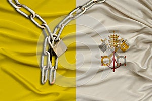 Iron chain and lock on vatican silk national flag with beautiful folds, the concept of a ban on tourism, political repression,